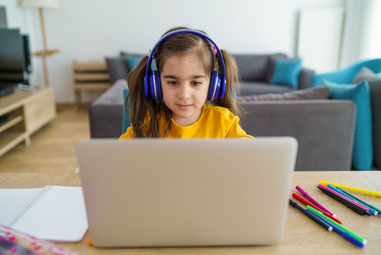 a young girl sitting at a laptop with headphones on.